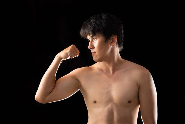 Muscle Boxer Vormgegeven aziatische man verhogen rechterhand posten zijaanzicht op zwarte achtergrond - Foto, afbeelding