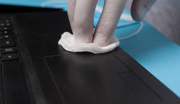 Egy közeli kép a fertőtlenítésről, amint egy laptopot tisztít fehér kesztyűben. A koronavírus-fertőzés megelőzése. - Fotó, kép