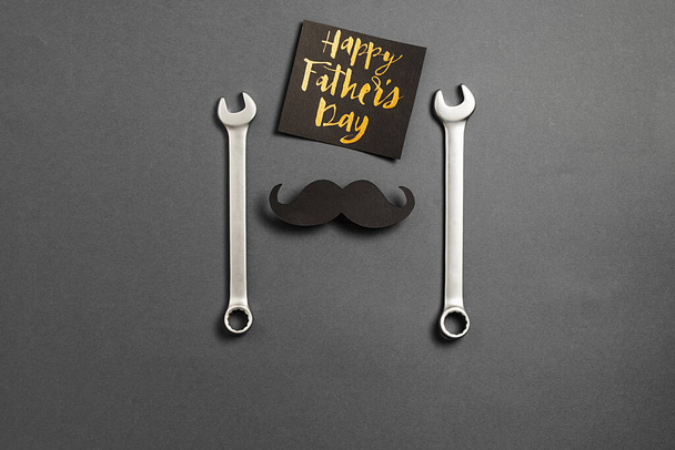 Combination wrenches, retro stylish black paper photo booth props moustaches, card with phrase happy father's day on grey background. Minimal style and holiday concept. Flat lay, copy space - Foto, Bild