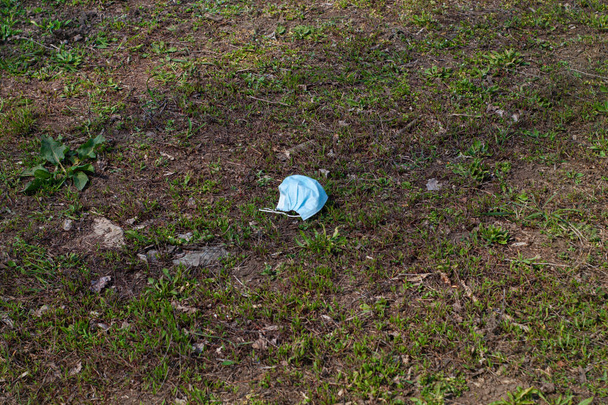 Używana maska medyczna na zielonej trawie w parku podczas kwarantanny COVID-19. Odpady niebezpieczne z ryzykiem wystąpienia choroby wirusowej. Śmieci z rozprzestrzeniającymi się zarazkami koronawirusów. Dzień wiosna widok ulicy podczas pandemii. - Zdjęcie, obraz