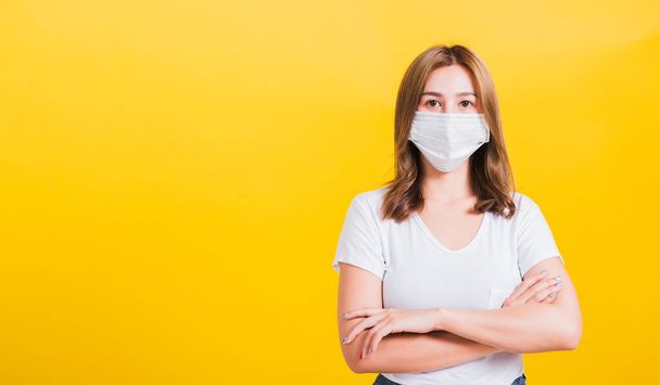 Portrait Asian beautiful young woman stand crossed arm wearing face mask protection filter dust pm2.5 anti-pollution, anti-smog, air pollution and COVID virus on a yellow background, with copy space - Фото, зображення