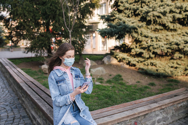 Girl in mask. Coronavirus theme. Women in the city, during quarantine. Alone in the city. Female use phone - Фото, изображение
