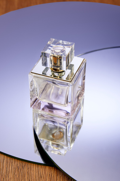 Butelka szklanych perfum na okrągłej fioletowej powierzchni lustra - Zdjęcie, obraz