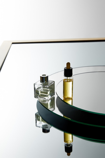 Hoge hoek weergave van parfumfles en serumfles op spiegeloppervlak  - Foto, afbeelding