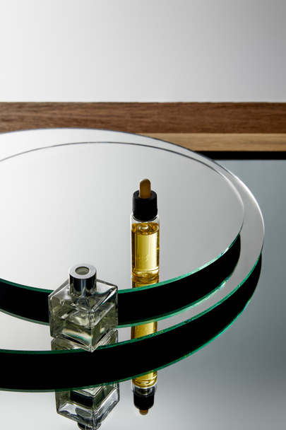 Вид под высоким углом на бутылку духов и сыворотку с маслом на зеркальную поверхность
  - Фото, изображение