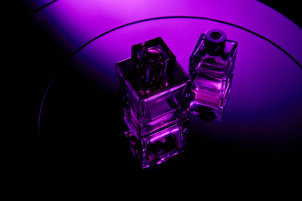 Hoge hoek weergave van paarse parfum flessen op ronde violette spiegel oppervlak - Foto, afbeelding