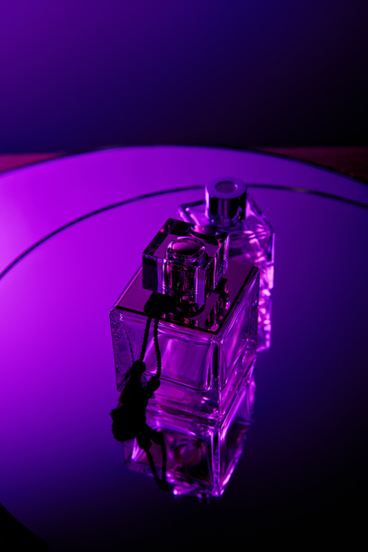 Vista superior de frascos de perfume sobre espejo violeta redondo superficie oscura
 - Foto, imagen
