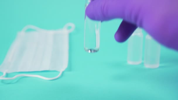 hand in surgical gloves puts a glass ampoule with a vaccine on a blue surface next to a medical protective mask - Séquence, vidéo