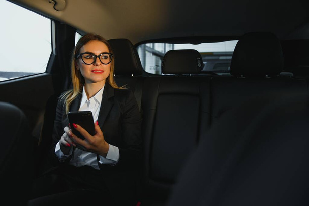 Some sort of interesting information. Smart businesswoman sits at backseat of the luxury car with black interior. - Фото, изображение