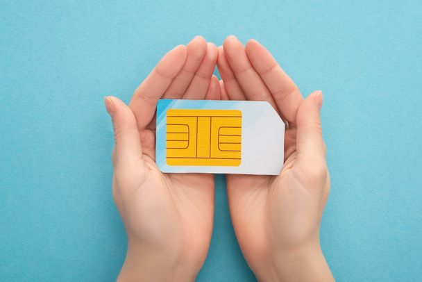 vista recortada de la mujer sosteniendo tarjeta SIM sobre fondo azul
 - Foto, imagen
