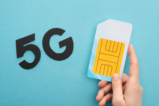 cropped view of woman holding sim card near 5g lettering on blue background - Zdjęcie, obraz