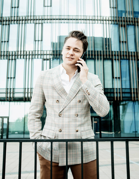 young businessman dressed in formal clothes standing outside a glass building and using mobile phone - Foto, afbeelding