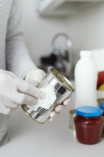 Großaufnahme eines Mannes in der Küche, der Latex-Handschuhe trägt, Konservendosen und Gläser reinigt, frisch gekauft, mit einem Desinfektionstuch - Foto, Bild