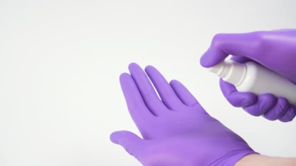 Uso de un spray desinfectante para el tratamiento higiénico de las manos en guantes protectores quirúrgicos azules sobre fondo blanco. Prevención de virus
 - Metraje, vídeo