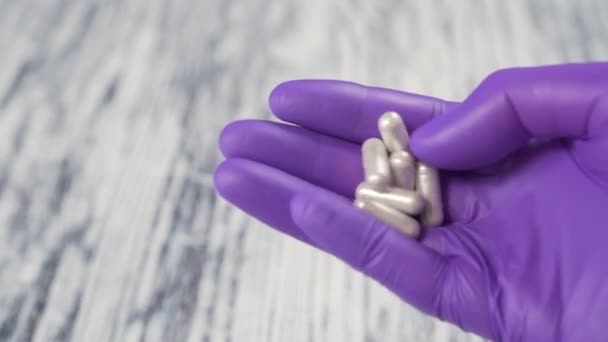 Several medical capsules in hand in blue protective surgical gloves on wooden background - Filmmaterial, Video