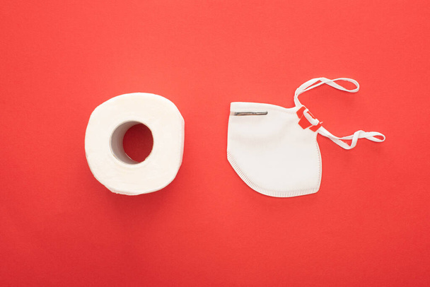 felső nézet fehér tiszta WC-papír tekercs és biztonsági maszk piros háttér - Fotó, kép