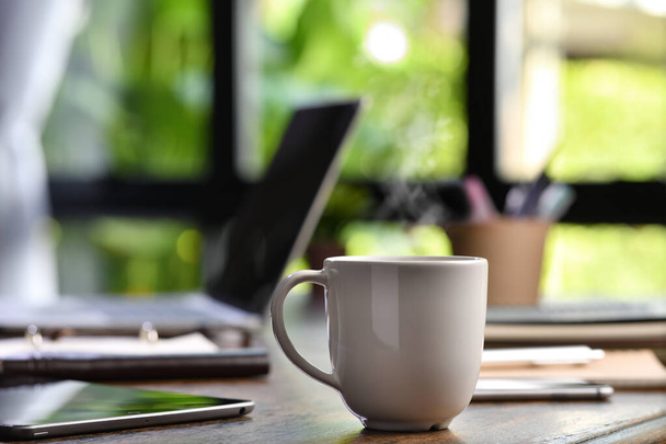 Una taza de café caliente y humeante en un escritorio con computadora portátil y gadget cuando el trabajo desde casa
 - Foto, Imagen
