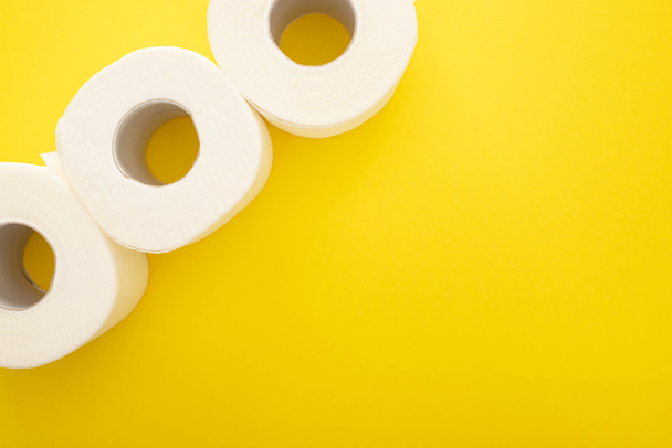 Draufsicht auf weiße Toilettenpapierrollen auf gelbem Hintergrund mit Kopierraum - Foto, Bild
