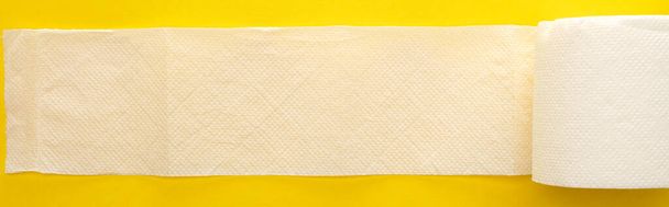 黄色の背景に展開されていない白いトイレットペーパーの上からの眺めパノラマ撮影 - 写真・画像
