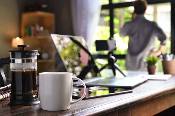 Кавова преса і чашка на робочому столі з людиною, яка працює з дому
 - Фото, зображення