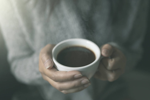 Primo piano delle mani femminili con una tazza di caffè caldo. alla luce del sole morbida del mattino. Bella ragazza in maglione grigio
. - Foto, immagini