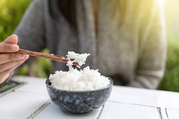 Asian women holding cooked jasmine rice bowls with chopsticks. Wearing a gray sweater. - Photo, Image