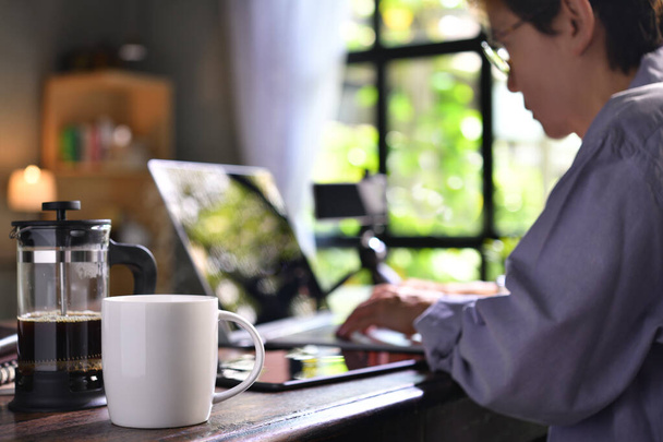 Una prensa de café y una taza en un escritorio con una persona que trabaja desde casa
 - Foto, imagen