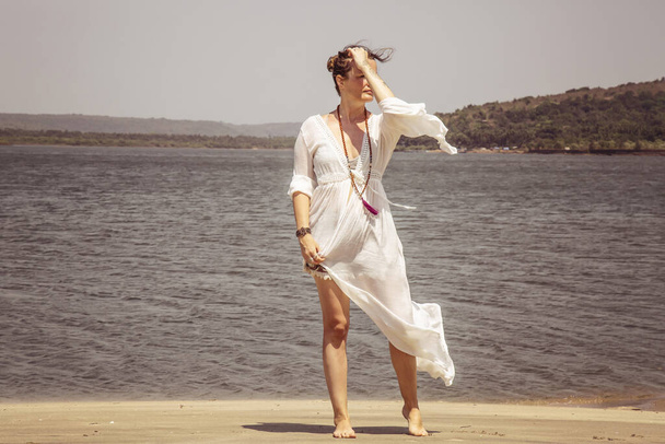 Nő fehér ruhában és mala nyaklánc a napfényes tengerparton a tenger mellett - Fotó, kép