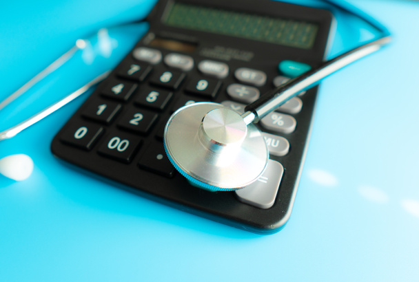 Calculadora e estetoscópio sobre o conceito de demonstração financeira para financiar o exame de saúde ou o custo dos cuidados de saúde
 - Foto, Imagem