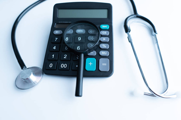 Concept of medical expenses or medical insurance for blog title and header. Stethoscope,white calculator and magnifying glass on wooden background. - Photo, Image