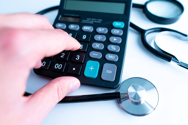 Selective focus Health care concept. Stethoscope on a calculator with Magnifying glass with effect light added. - Photo, Image