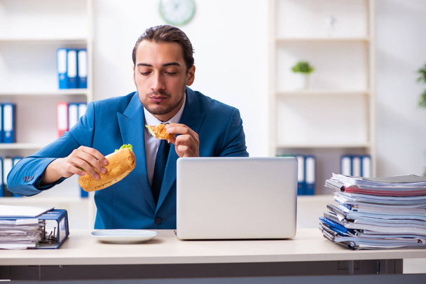 Jeune employé masculin prenant son petit déjeuner sur le lieu de travail
 - Photo, image