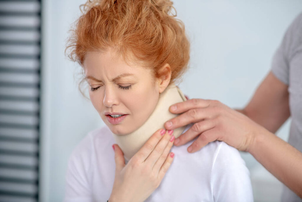 男性理学療法士の手は首のフィクサーを調べます,痛みから顔をしかめる女性患者 - 写真・画像