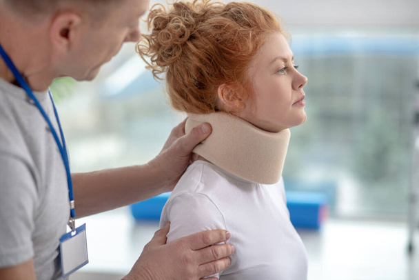 Male physiotherapist examining neck fixator of female patient - Фото, зображення