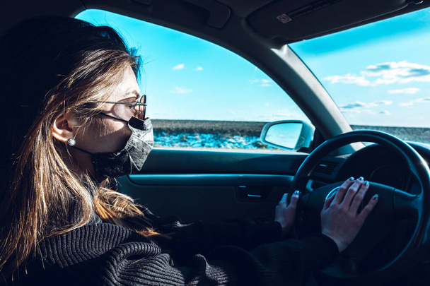 A brunette girl drives a car in a medical mask, fearing infection. - Fotó, kép