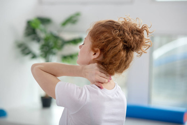 Red-haired female patient massaging her painful neck - Valokuva, kuva