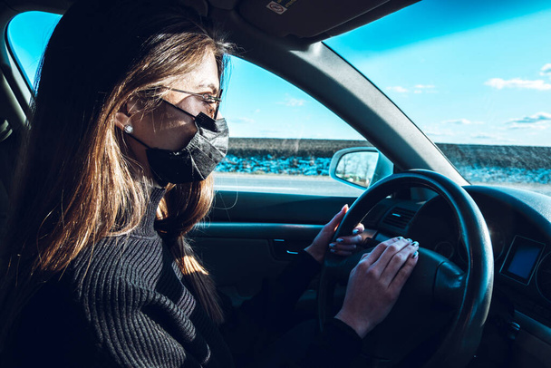 A brunette girl drives a car in a medical mask, fearing infection. - Photo, Image