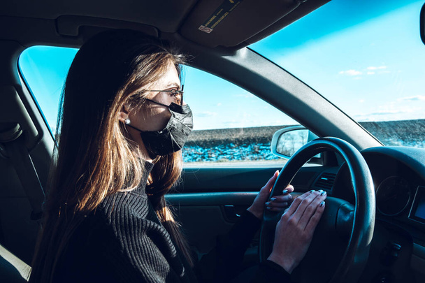 A brunette girl drives a car in a medical mask, fearing infection. - Photo, Image