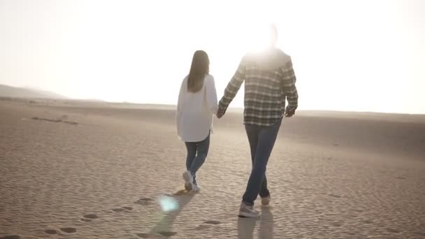 Rara vista de pareja cogida de la mano caminando en relación romántica bajo el sol y el cielo azul en el desierto. Dos jóvenes amantes caminando por la arena del desierto en ropa casual, tomados de la mano. Bengalas de lente
 - Imágenes, Vídeo