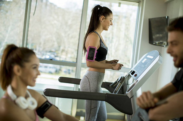 Hübsche junge Frau benutzt Laufband in modernem Fitnessstudio - Foto, Bild