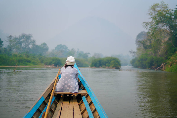 Kleines Holzboot auf einem wilden tropischen Fluss im grünen Dschungel, vor dem eine Frau sitzt und friedlich die Landschaft betrachtet. Blaues Kanu erkundet die Natur. - Foto, Bild