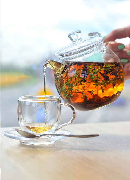 Ze skleněné konvice nalijte čaj do skleněného kelímku na světlém pozadí - Fotografie, Obrázek