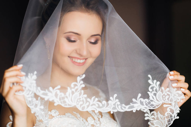 a noiva cobriu seu rosto com um véu de casamento e olha para baixo. maquiagem bonita e sorriso. - Foto, Imagem