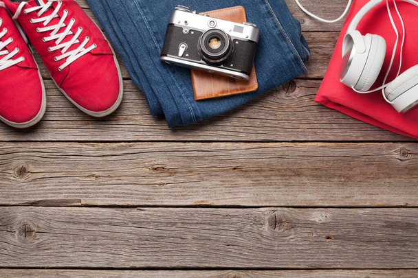 Одяг та аксесуари. Кросівки, джинси і фотоапарат. Міське вбрання для повсякденних або туристичних відпусток на дерев'яному тлі з копіювальним простором. Вид зверху плоский лежав
 - Фото, зображення