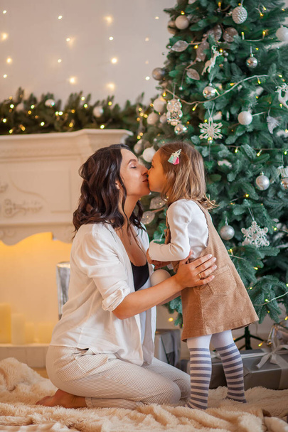 mom kisses daughter near the Christmas tree at home - Φωτογραφία, εικόνα