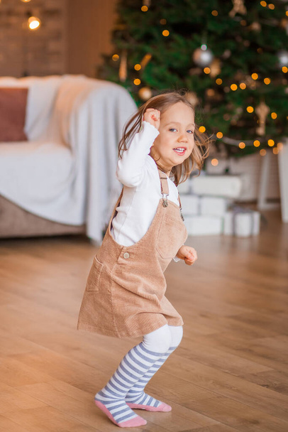 little girl plays near the christmas tree lights - Foto, afbeelding