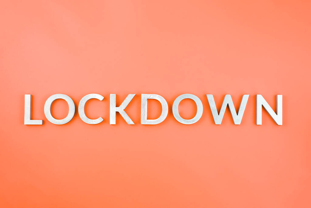 the word lockdown laid with brushed aluminium metal letters on lush lava orange color background - Photo, Image