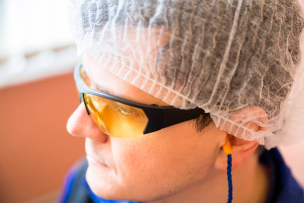 Close-up van de mens in speciale kleding houdt - in een hoed, beschermende gele bril, oordopjes in een voedselverwerkende bedrijf. Voorschriften voor kleding in de voedselproductie. - Foto, afbeelding
