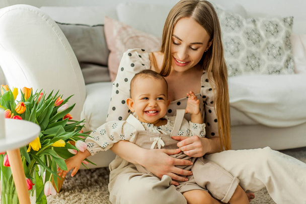 Happy mom and mulatto girl in home interior. Mothers Day. Baby. - Foto, afbeelding