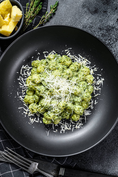 Gnocchi with basil spinach sauce and Parmesan. Italian potato paste. Black background. Top view. - Foto, afbeelding